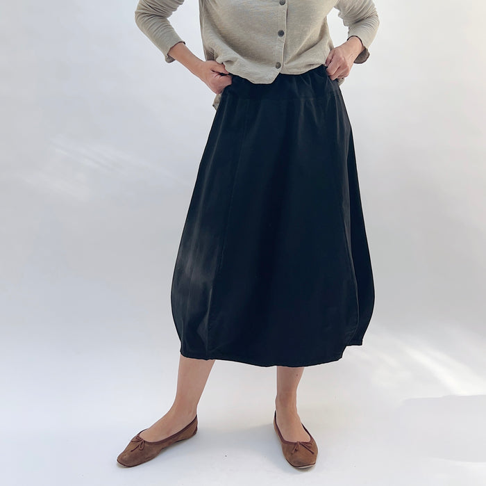 Rib Yoke Skirt in Black, front view, model adjusting elastic waistband, styled with a beige cardigan and brown flats