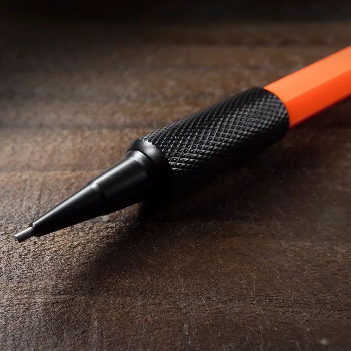 A close-up of a mechanical pencil with a textured black handle and bright orange shaft, resting on a dark wooden surface.
