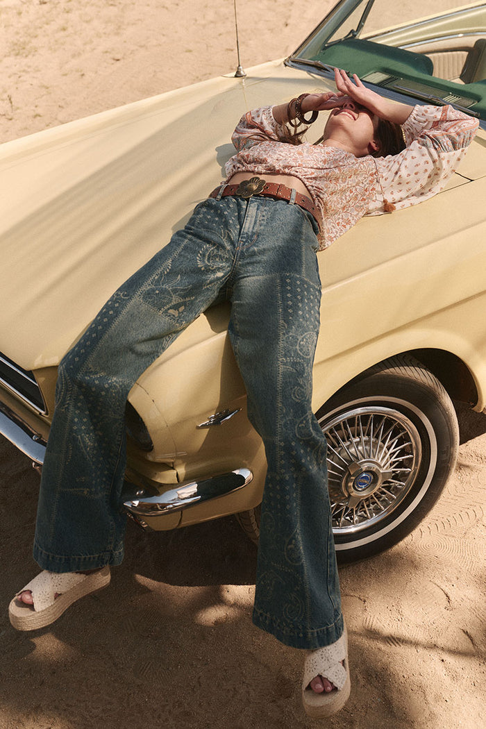 Front view of Road Trip Denim Jean in Bandana, laser-print wide leg, styled with boho blouse leaning on vintage car