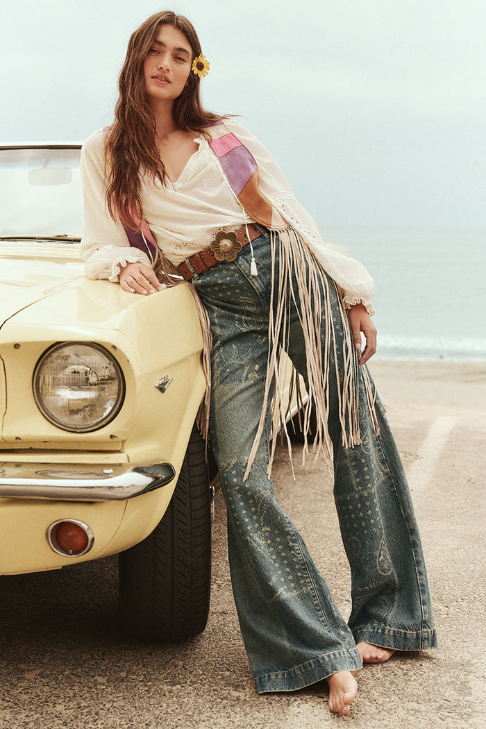 Front view of laser-printed bandana wide leg denim jeans with belt loops, styled with fringe belt beside vintage car