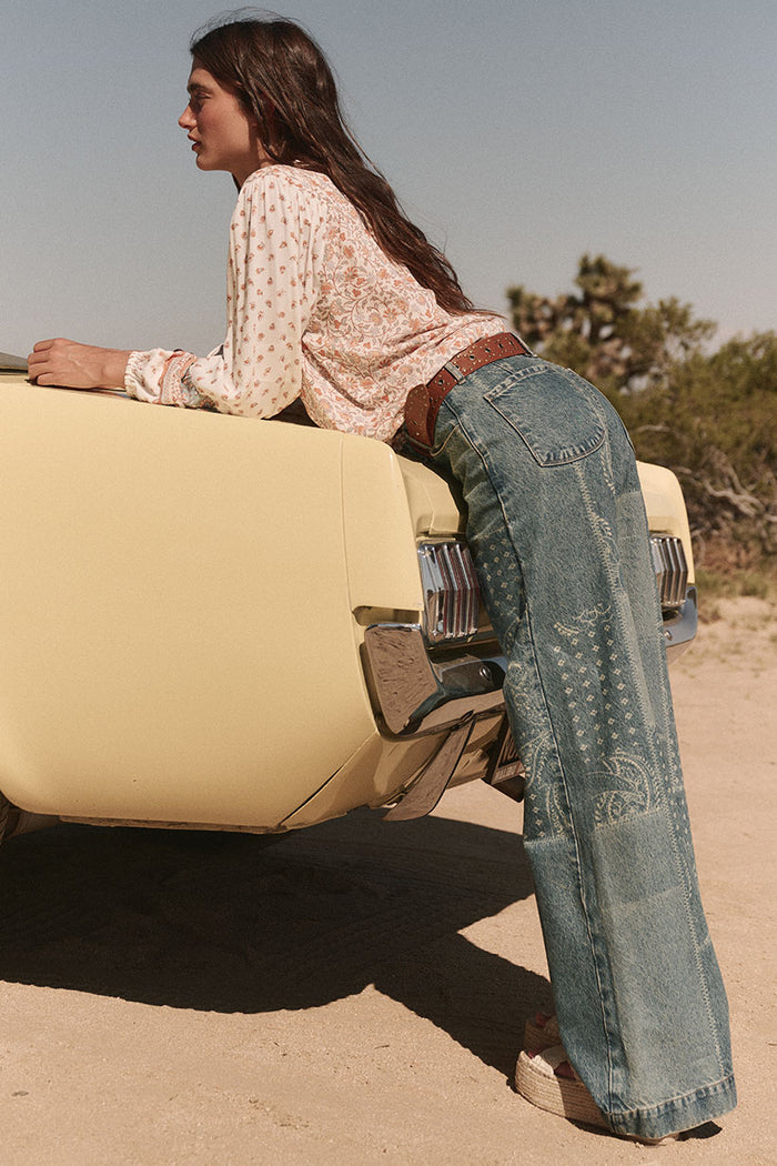 Back view of bandana laser-print wide-leg denim jeans with back patch pockets and belt loops, desert setting