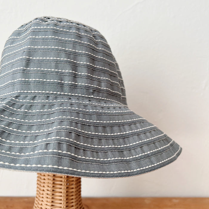 Close-up of sage ribbon hat fabric showing horizontal white running stitch detail across a wide floppy brim