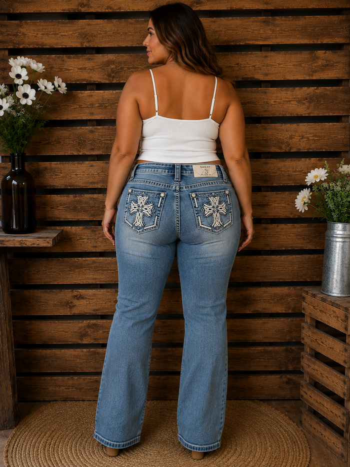 Woman wearing blue jeans with decorative stitching against a wooden wall.