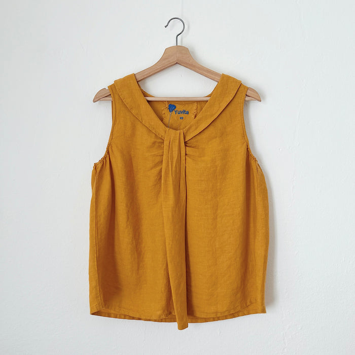 A sleeveless, mustard yellow linen top hanging on a wooden hanger against a white background.