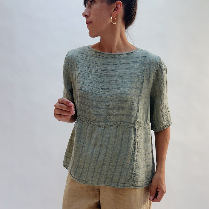 Model wearing the Seamed Boxy Striped Top in Balsam Green, a relaxed short-sleeve top with a textured stripe pattern, seamed waist detail, and crew neck, styled with tan linen pants looking off to the side