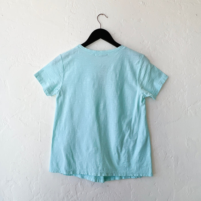 Light blue t-shirt on a black hanger against a white wall, viewed from behind
