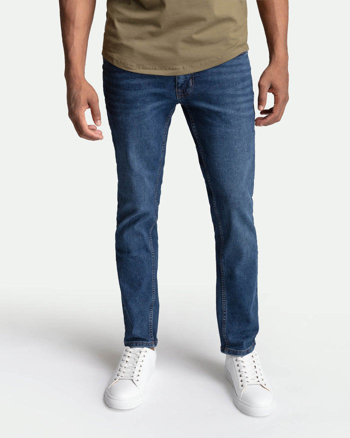 Man wearing medium blue skinny fit jeans with a tan t-shirt and white sneakers.