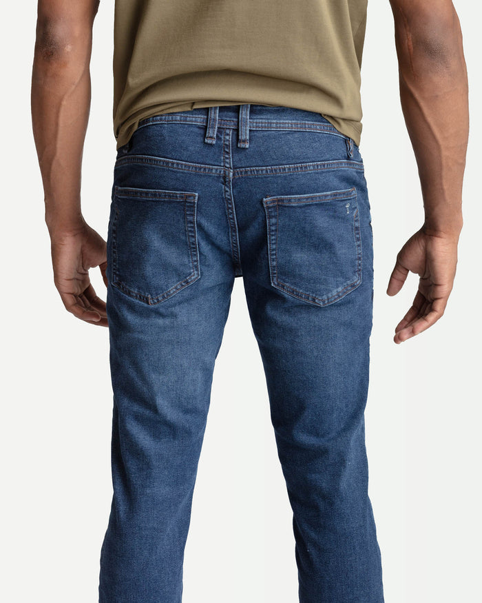 Man wearing medium blue skinny fit jeans with back pockets, paired with olive t-shirt.