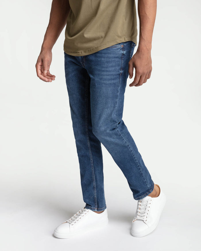 Medium blue skinny fit jeans on a man wearing a tan t-shirt and white sneakers.