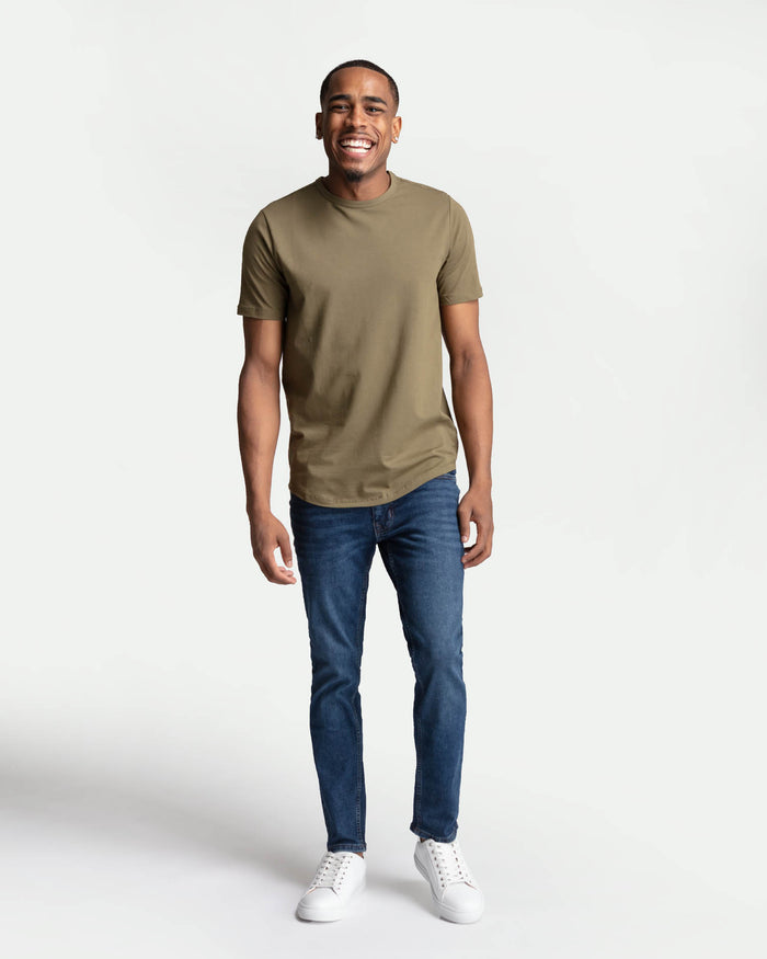 Man wearing olive-green short-sleeve t-shirt and medium blue skinny fit jeans with white sneakers.