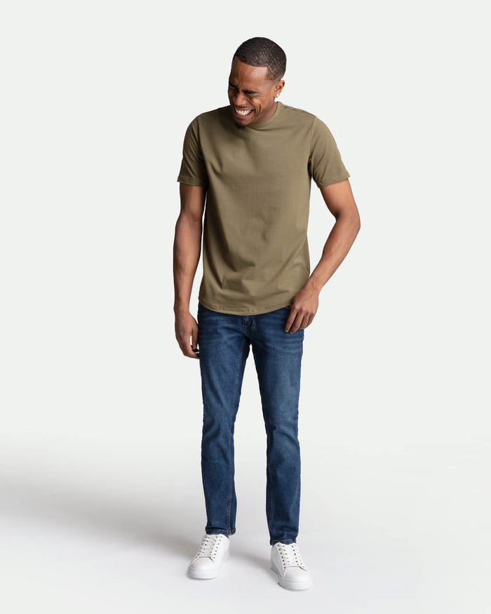 Man wearing olive-green short-sleeve t-shirt and medium blue skinny-fit jeans with white sneakers.