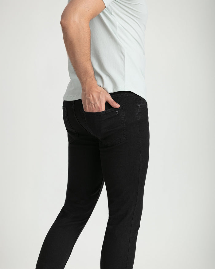 Man wearing black skinny fit jeans with white t-shirt, side view showing pocket detail.