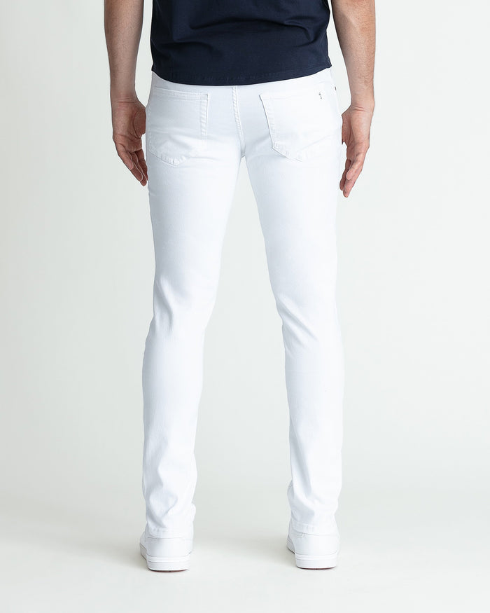White skinny fit jeans on male model wearing navy top and white sneakers.