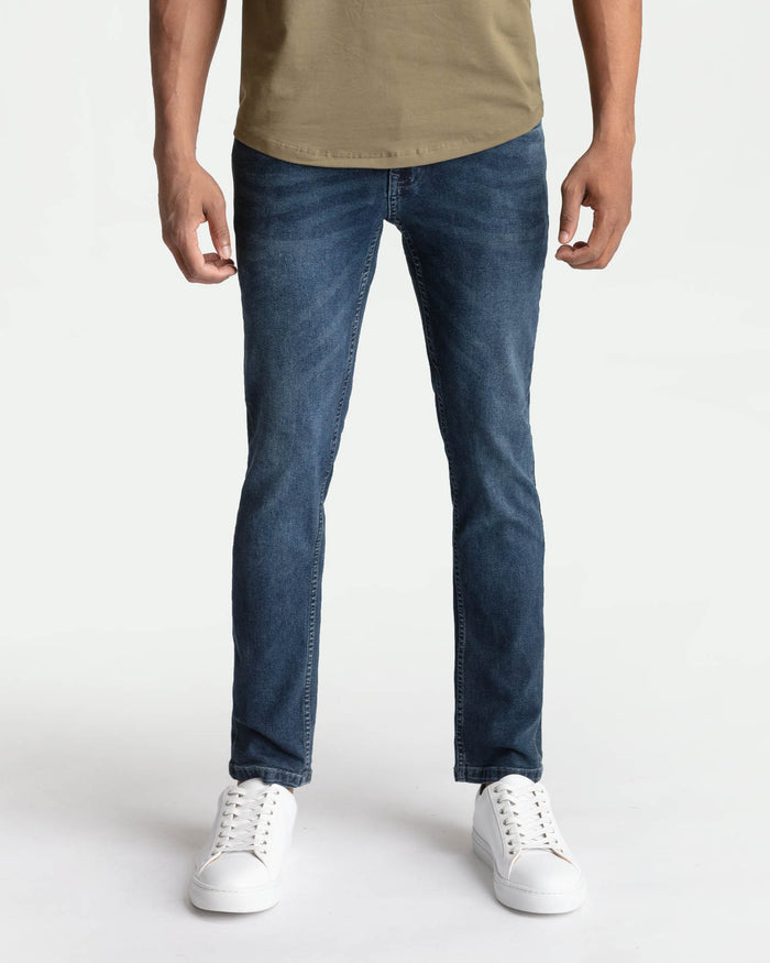 Man wearing midnight blue skinny fit jeans with a tan shirt and white sneakers.