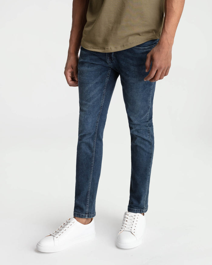 Skinny fit midnight blue jeans on model wearing tan t-shirt and white sneakers.