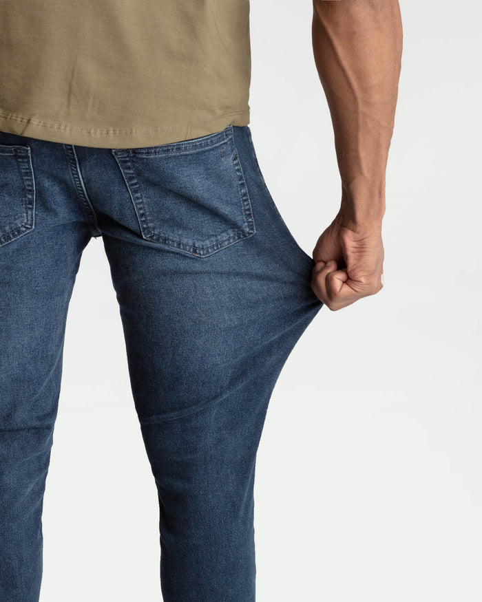 Man wearing midnight blue skinny fit jeans with beige shirt, showing back pocket detail and fit.
