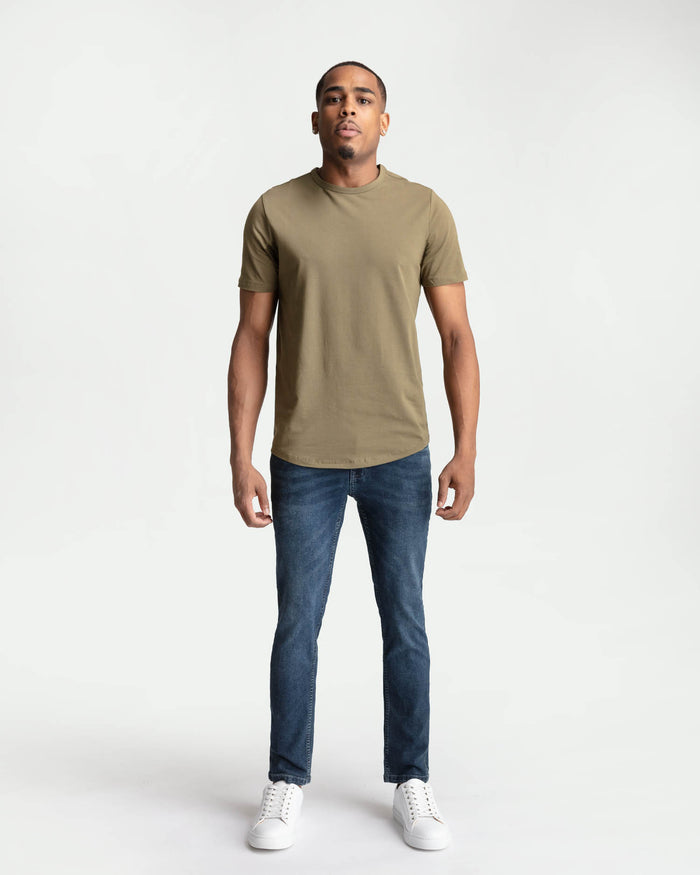 Man wearing tan short-sleeve t-shirt and dark blue skinny fit jeans with white sneakers.