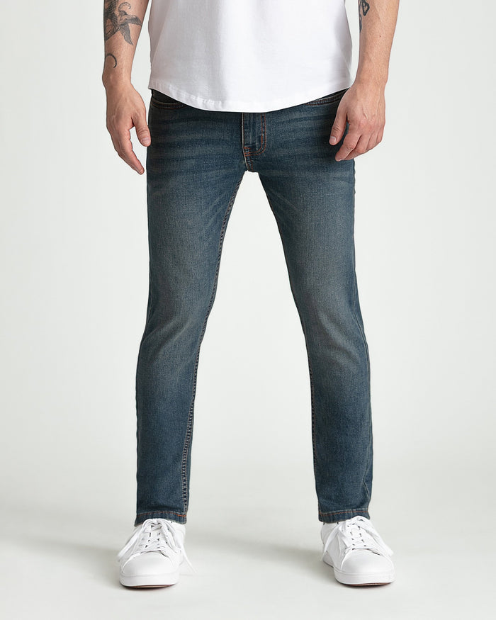 Dark tinted skinny fit jeans with orange stitching, worn with white t-shirt and white sneakers.