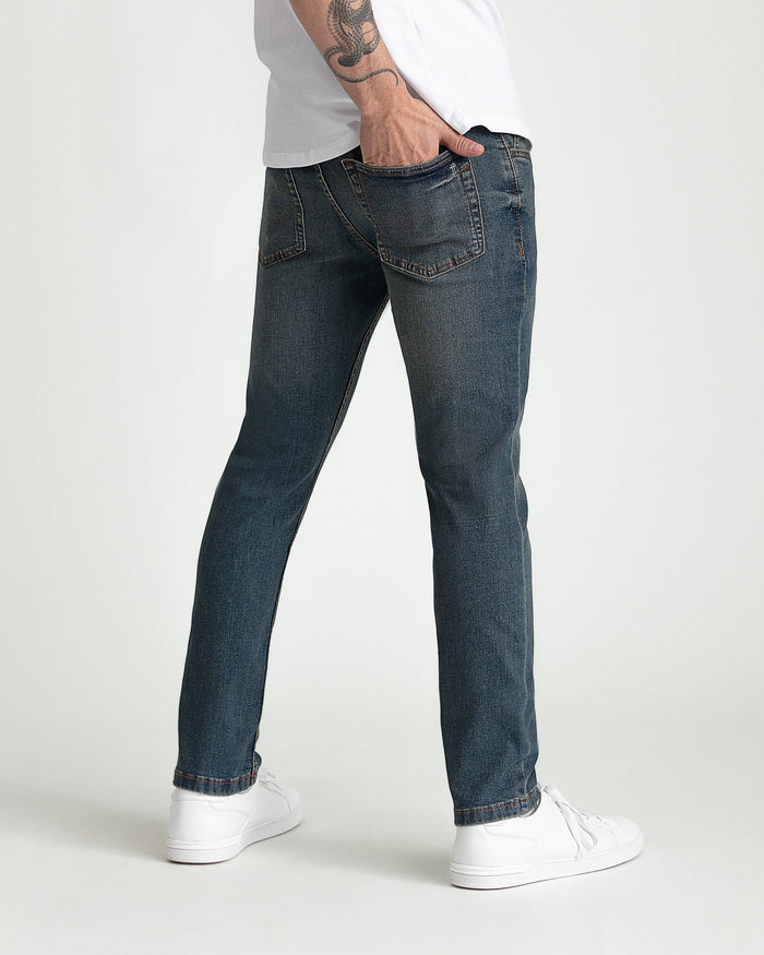 Dark tinted denim jeans with skinny fit cut and five-pocket styling worn with white sneakers.