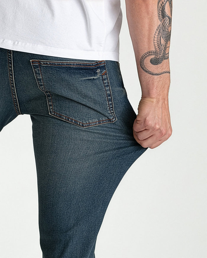 Dark tinted skinny fit jeans with brown stitching and back pocket detail on male model.