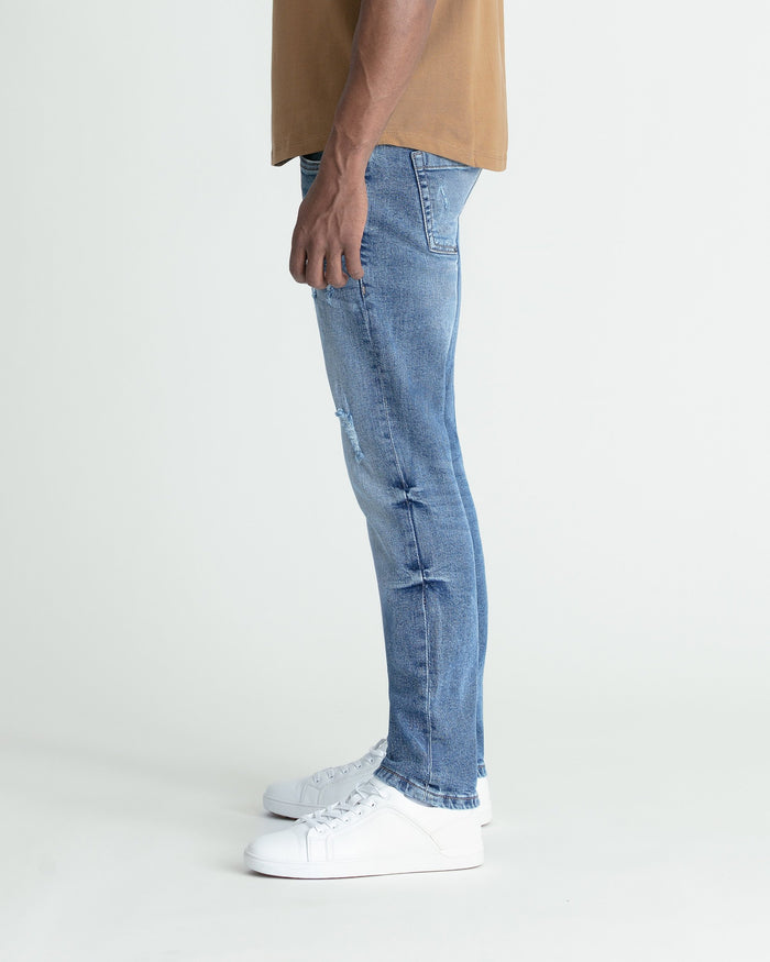 Medium blue skinny fit jeans with ripped details on the thigh, styled with white sneakers.