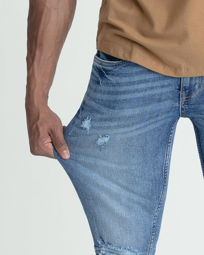 Medium blue skinny fit jeans with ripped details on the thighs and lower leg.