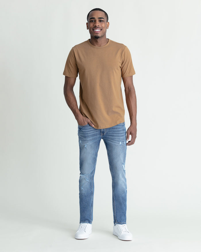 Man wearing tan crew neck t-shirt and medium blue skinny fit jeans with ripped details at thighs.
