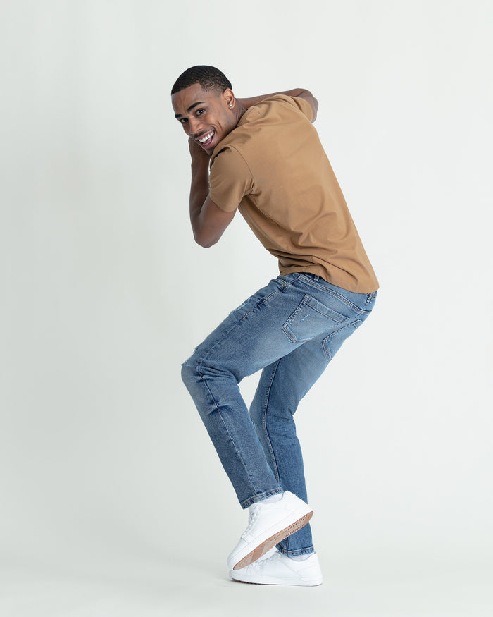 Medium blue skinny fit jeans with ripped knee detail, styled with tan hoodie and white sneakers.