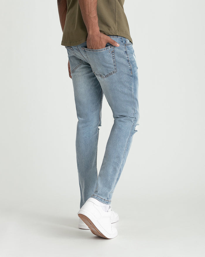 Light blue skinny fit jeans with ripped knee detail and frayed hem on model wearing white sneakers.