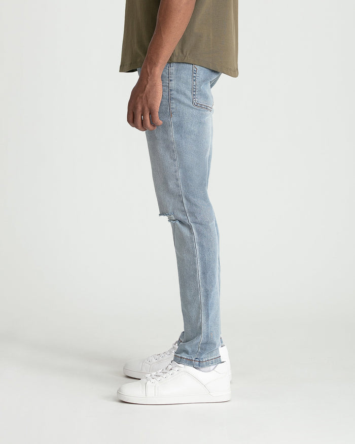 Light blue skinny fit jeans with ripped details on thigh, worn with olive shirt and white sneakers.