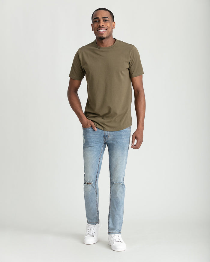 Man wearing olive-green t-shirt and light-wash skinny fit jeans with ripped knees and white sneakers.