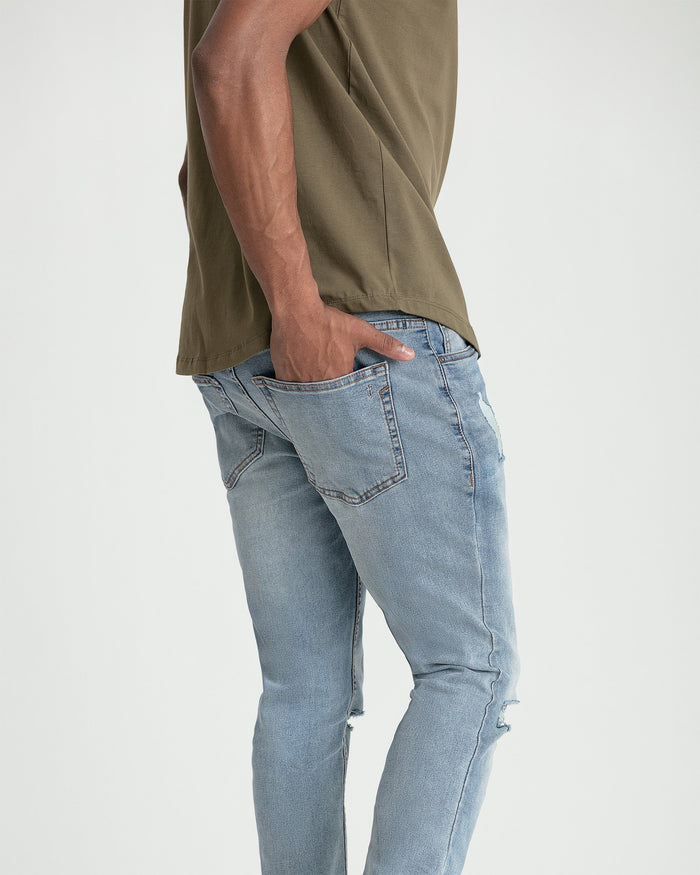 Light blue skinny fit jeans with ripped details at the knees, shown on model wearing olive shirt.