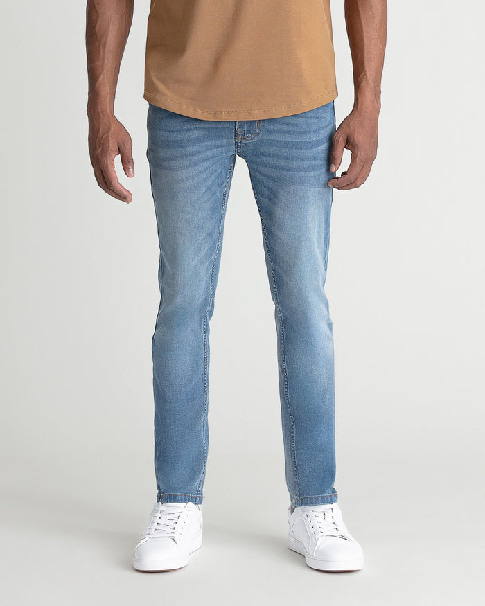 Man wearing light indigo skinny fit jeans with tan shirt and white sneakers.