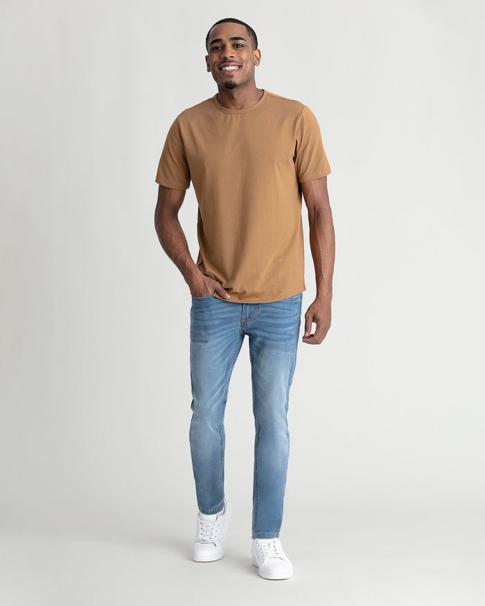 Man wearing tan t-shirt and light blue skinny fit jeans with white sneakers.