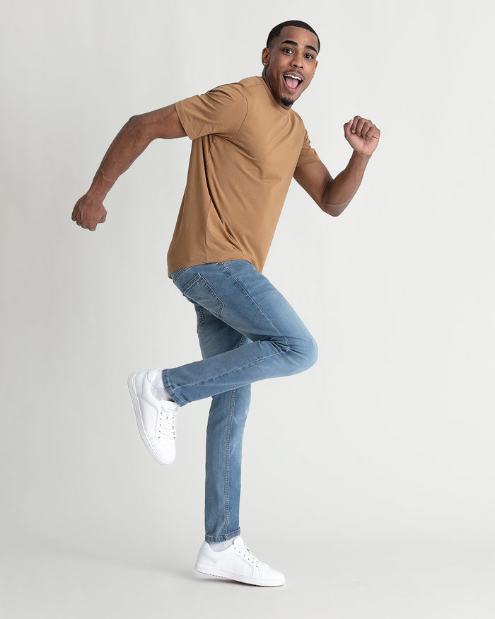 Man wearing tan t-shirt and light indigo skinny fit jeans with white sneakers.