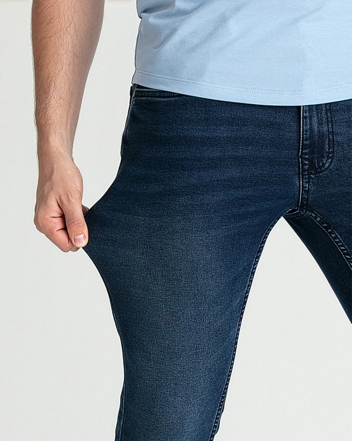 Man wearing dark blue skinny fit jeans with light blue t-shirt, detail of thigh and waistband.
