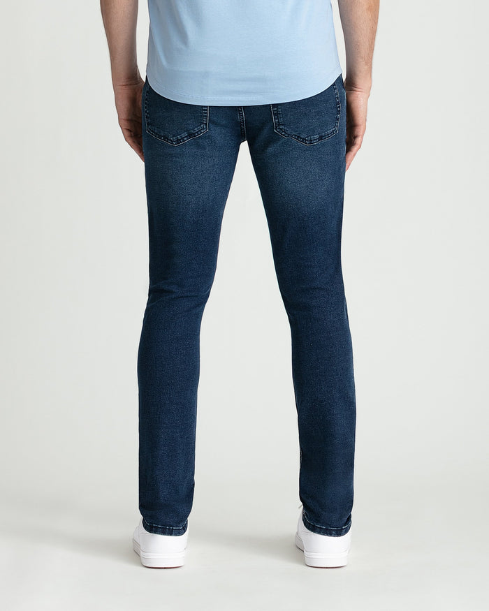 Man wearing light blue t-shirt and dark blue skinny fit jeans with white sneakers, rear view.