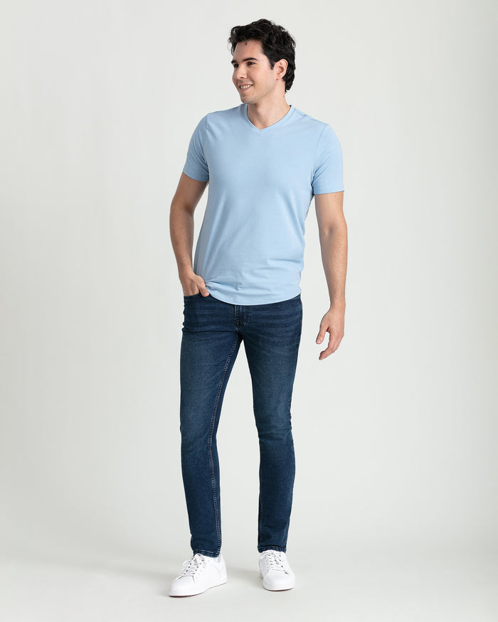 Man wearing light blue v-neck t-shirt and dark blue skinny fit jeans with white sneakers.