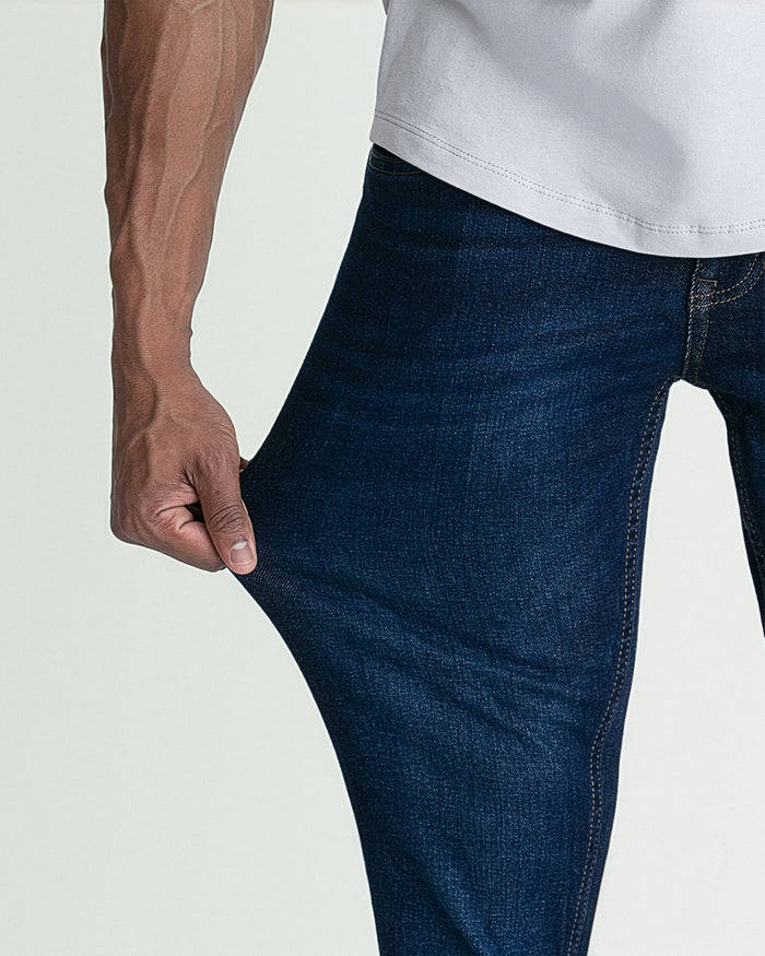 Dark blue skinny fit jeans with visible stitching, worn with a white shirt and brown long-sleeve top.
