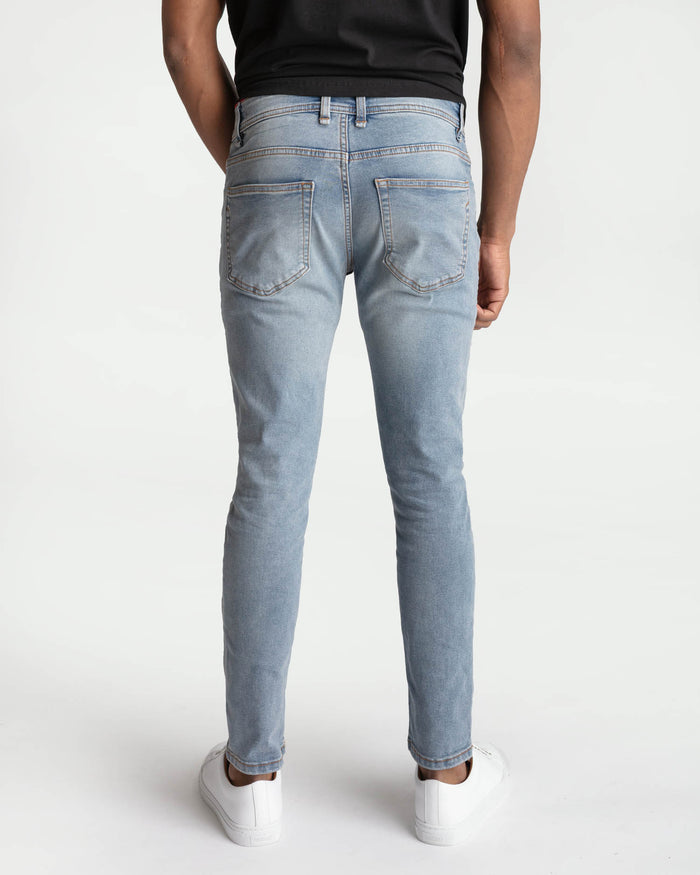 Light blue skinny fit jeans with five-pocket styling and back patch pockets, shown from behind on a model.