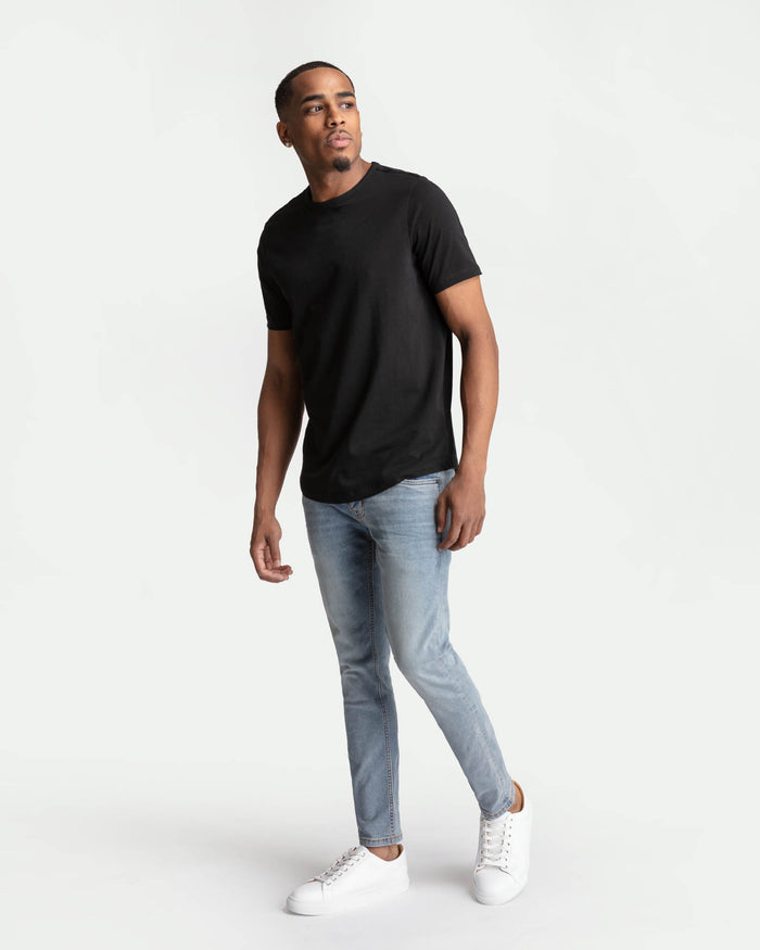 Man wearing black short-sleeve t-shirt and light blue skinny fit jeans with white sneakers.