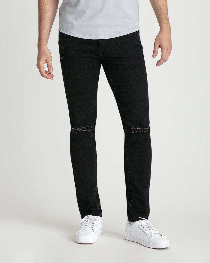 Black skinny fit jeans with ripped knee details worn with white sneakers and gray t-shirt.