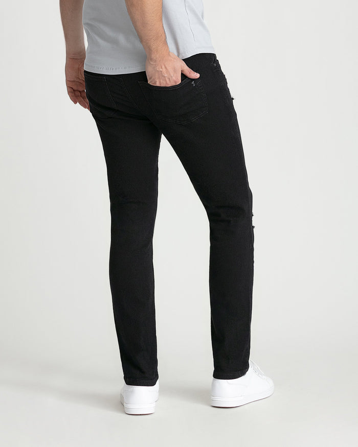Black skinny fit jeans with ripped details on thighs, shown on male model with white sneakers.