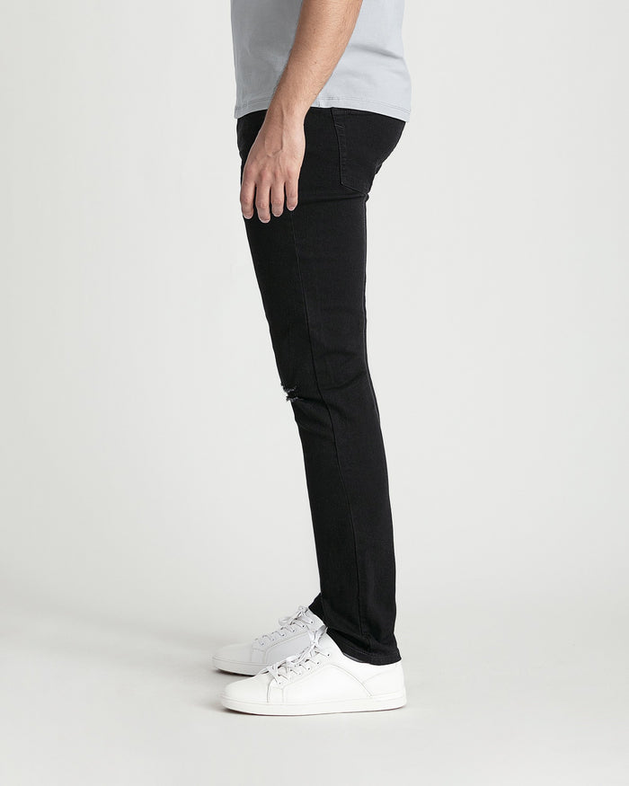 Black skinny fit jeans with ripped thigh detail, shown on model wearing white sneakers.