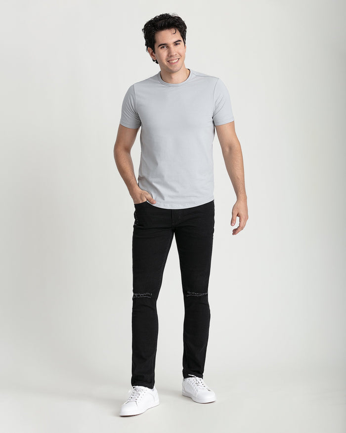 Man wearing light gray t-shirt and black skinny fit jeans with ripped knee details and white sneakers.