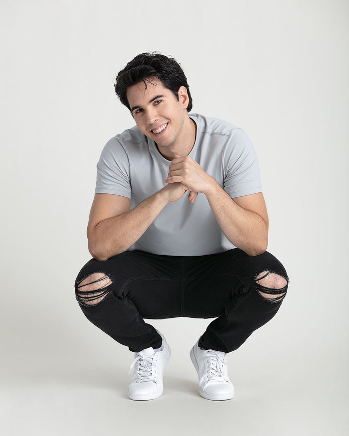 Man wearing gray t-shirt and black skinny jeans with ripped knees and white sneakers.