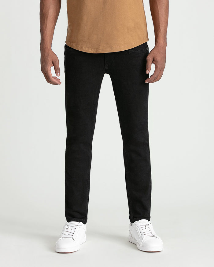 Man wearing black skinny fit jeans with tan t-shirt and white sneakers.