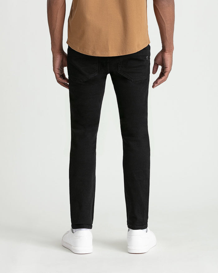 Black skinny fit jeans on male model wearing tan shirt and white sneakers.