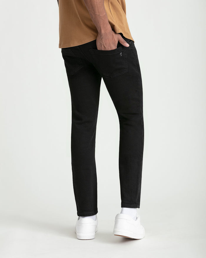 Black skinny fit jeans with back pocket detail, worn with tan shirt and white sneakers.
