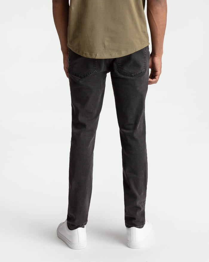 Man wearing tan t-shirt and faded black skinny fit jeans, shown from behind.